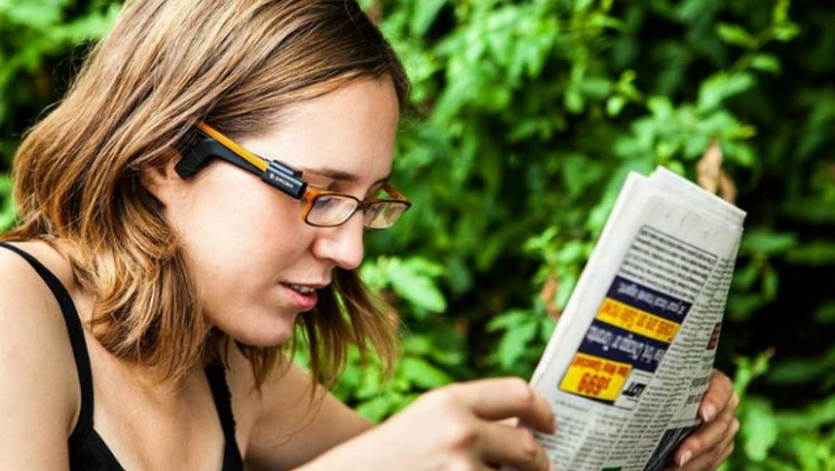 Image of a woman wearing the OrCam reading a newspaper