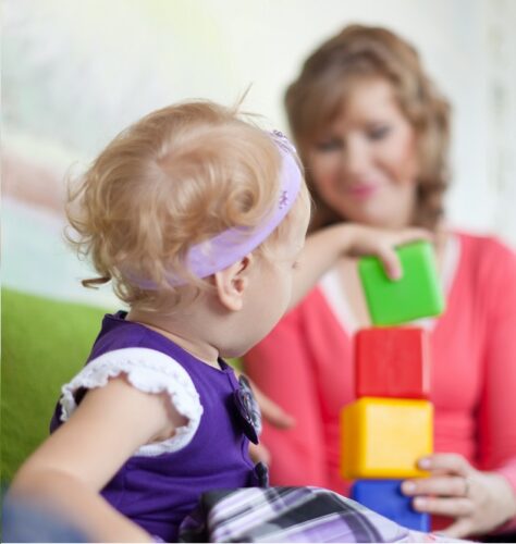 A small girl playing with building blocks as her mother watches on