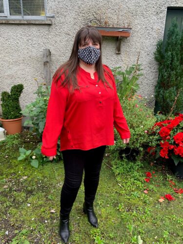 Geraldine Conway stands in a Garden and poses for a picture while wearing a face mask