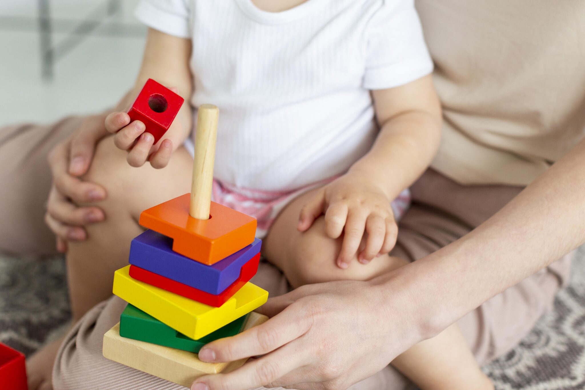 A child sitting on a parent's lap as they put block pieces onto a children's toy