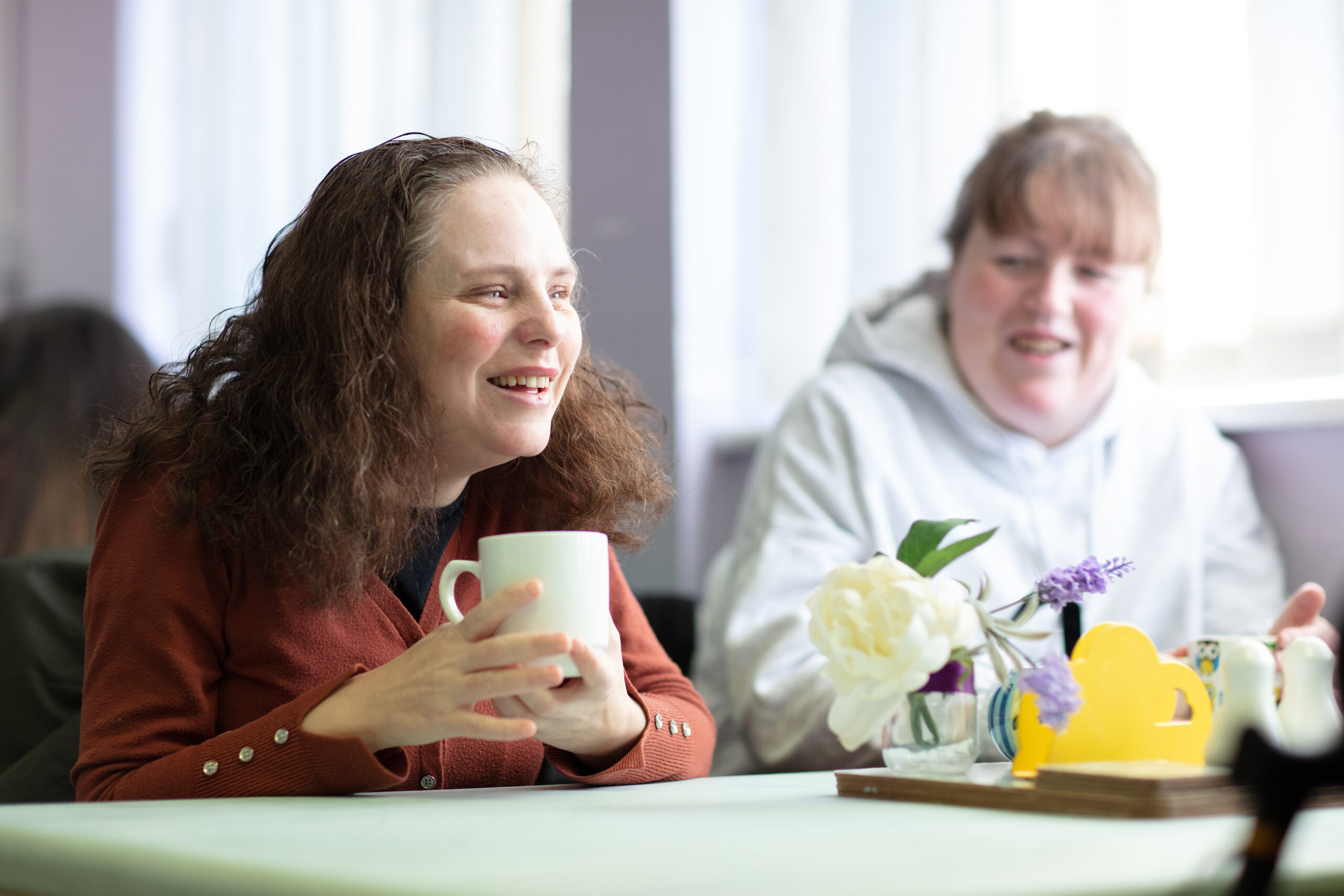 Two female NCBI service users laughing as they engage in conversation while sitting at a coffee table