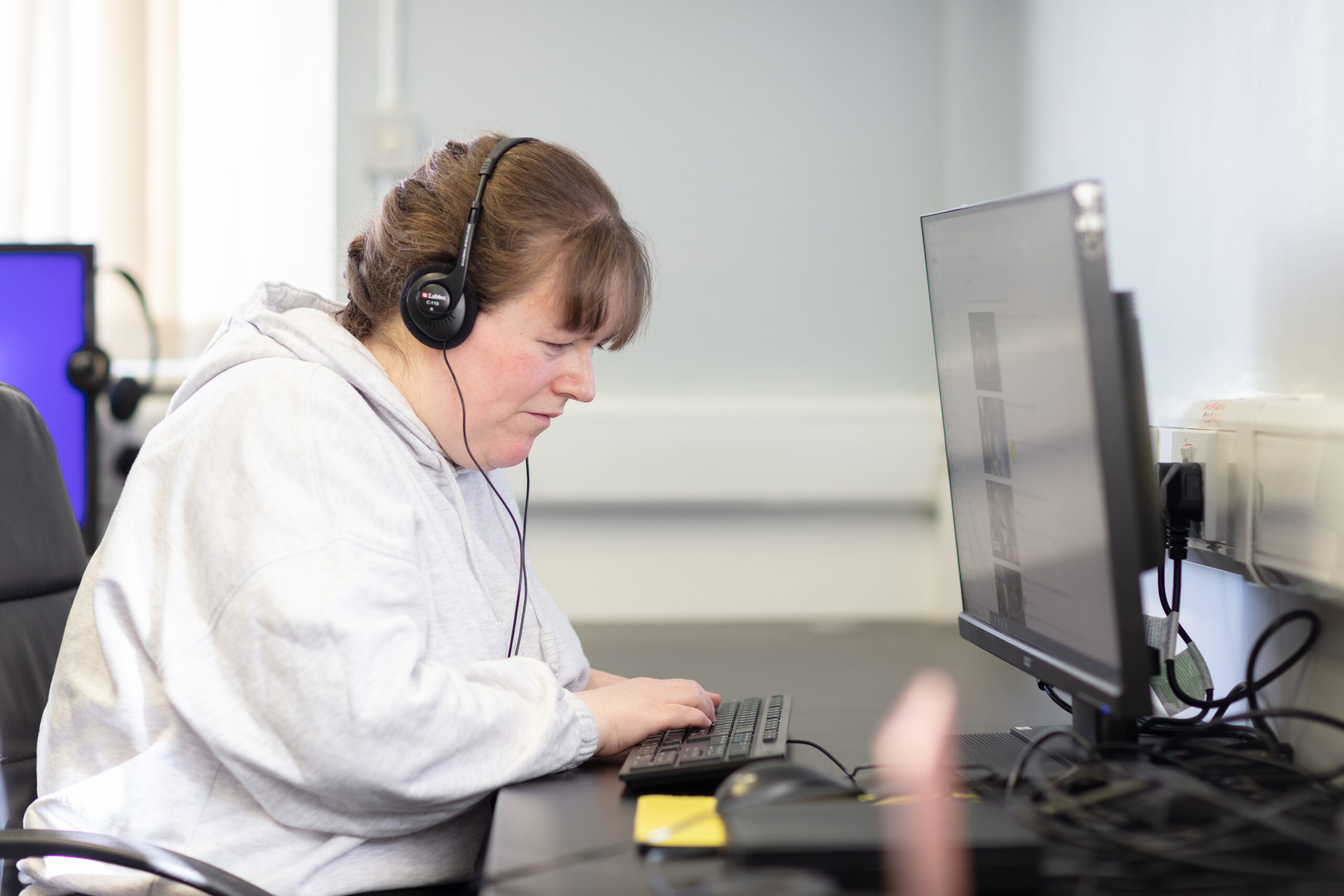An NCBI service user typing on a keyboard as they listen to audio through a pair of headphones