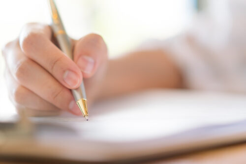 A close up picture of a hand holding a pen as a person writes onto a piece of paper