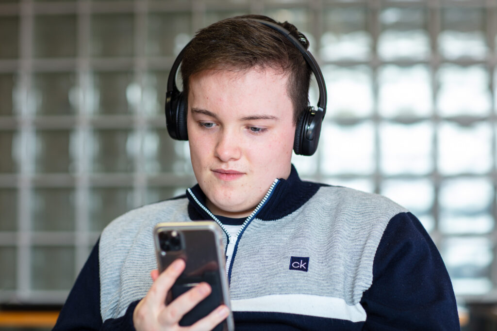 A young man who is wearing headphones while using accessible technology to read the screen on his smartphone