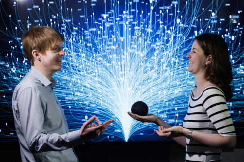 NCBI service users ex Rose of Tralee Aine Sullivan and comedian Robbie Ford standing face to face and laughing in front of a black and glowing blue background at the launch of myNCBI Smart Hub