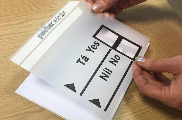 A person's hands holding a tactile voting template over a piece of paper. These templates are currently in use during times of voting for people who are blind or vision impaired.