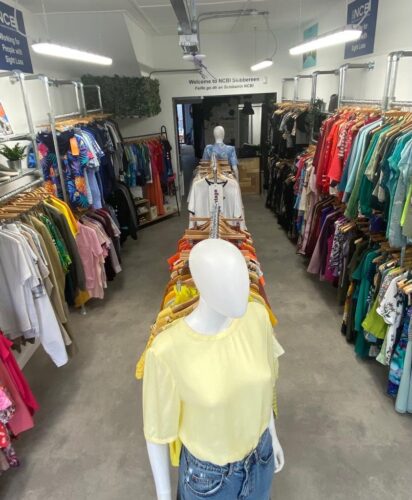 This wide shot inside NCBI Skibbereen shows colourful clothing on the left, right and middle of the store.