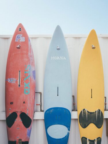 Photo of three surf boards standing up next to each other. The surf boards begin with a red one on the left, a blue one in the middle and a yellow one on the right.