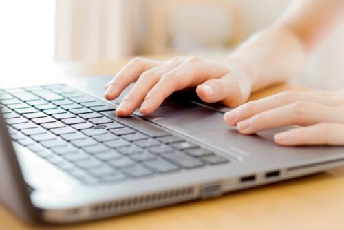 A person's two hands are on a laptop touch pad and on the space bar of the keyboard