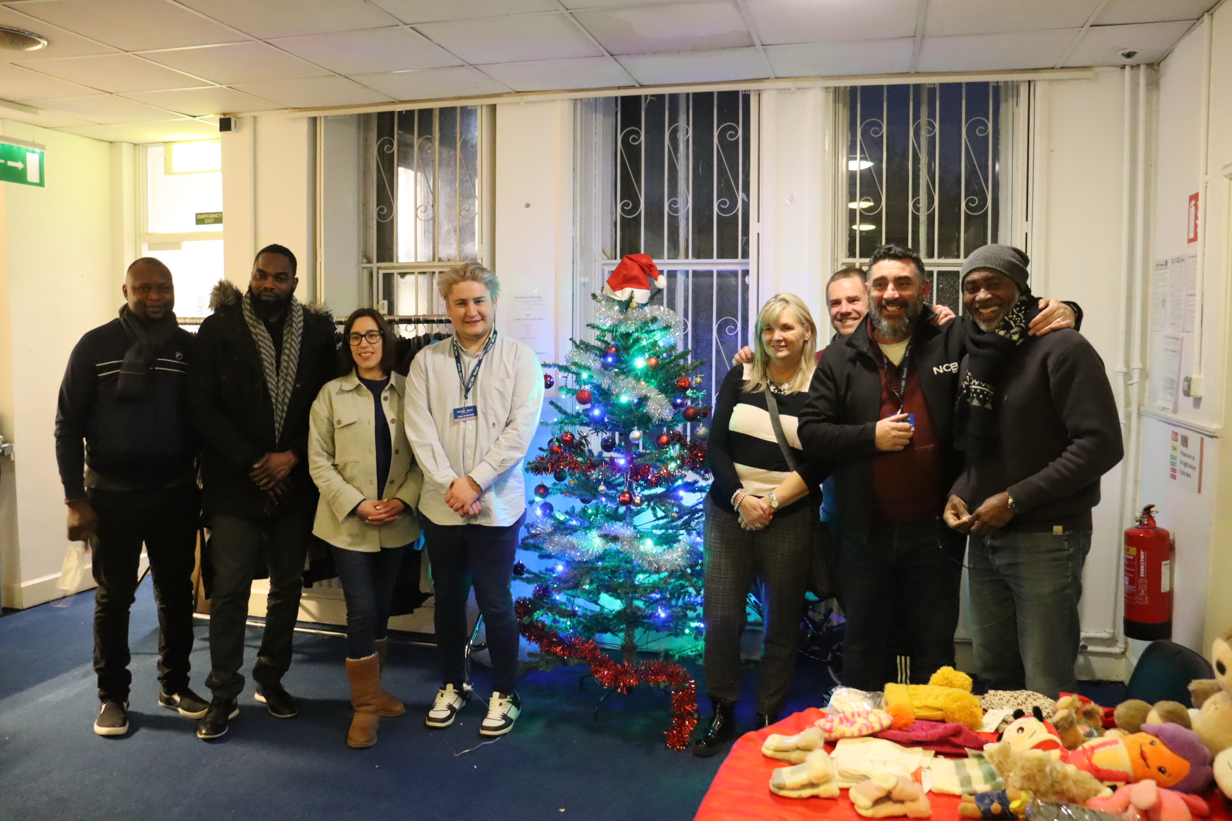 NCBI Retail staff alongside members of staff at Depaul's housing facility in north inner-city Dublin who worked together at the NCBI Retail pop-up store providing free clothing to Depaul service users on Wednesday 14th December. The group are all standing beside a Christmas tree and a clothing rail.