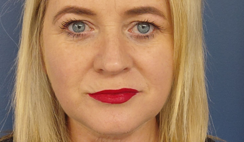A close up image of Geraldine Cussen's face as she stands in front of a blue wall. Geraldine has blonde hair and is wearing red lipstick.