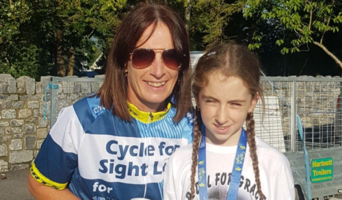 Mary O'Sullivan stands to the left of her 12-year-old daughter Grace. Mary is wearing a blue and white cycling top, which Grace is wearing an oversized white t-shirt and has a medal around her neck.