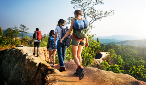 A family of backpackers are all wearing hiking gear and are walking along a nature trail which runs through a forest.