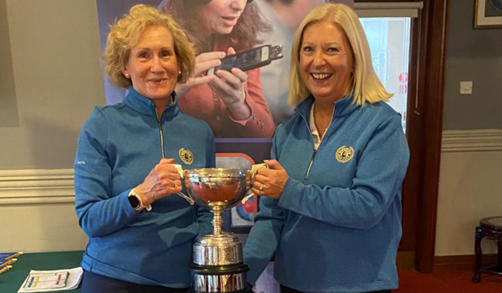 Mary Bell and Catherine Monaghan who bagged the big prize in the ladies’ event, the Granard Cup are standing together, wearing matching light blie jackets, and are holding their trophy in front of an NCBI banner.